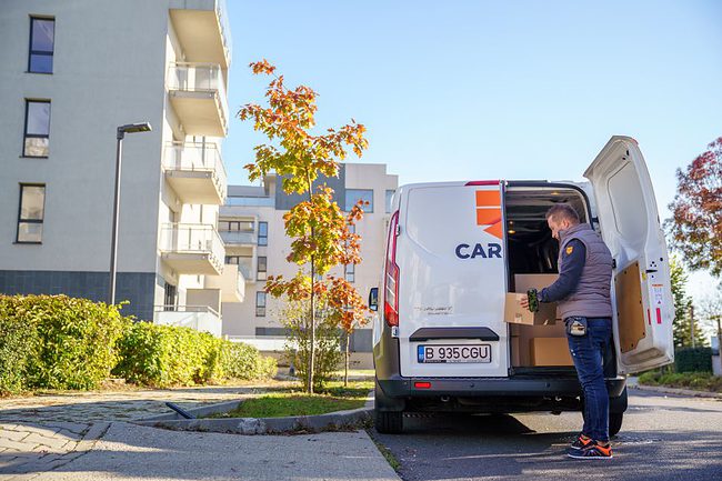 barbat cu colet in mana langa masina de curierat